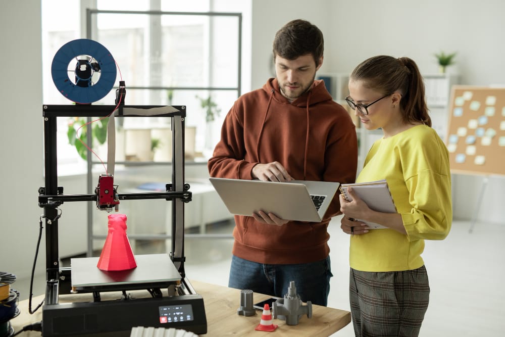 Two Young Creative Designers Standing in Front of 3D Printer