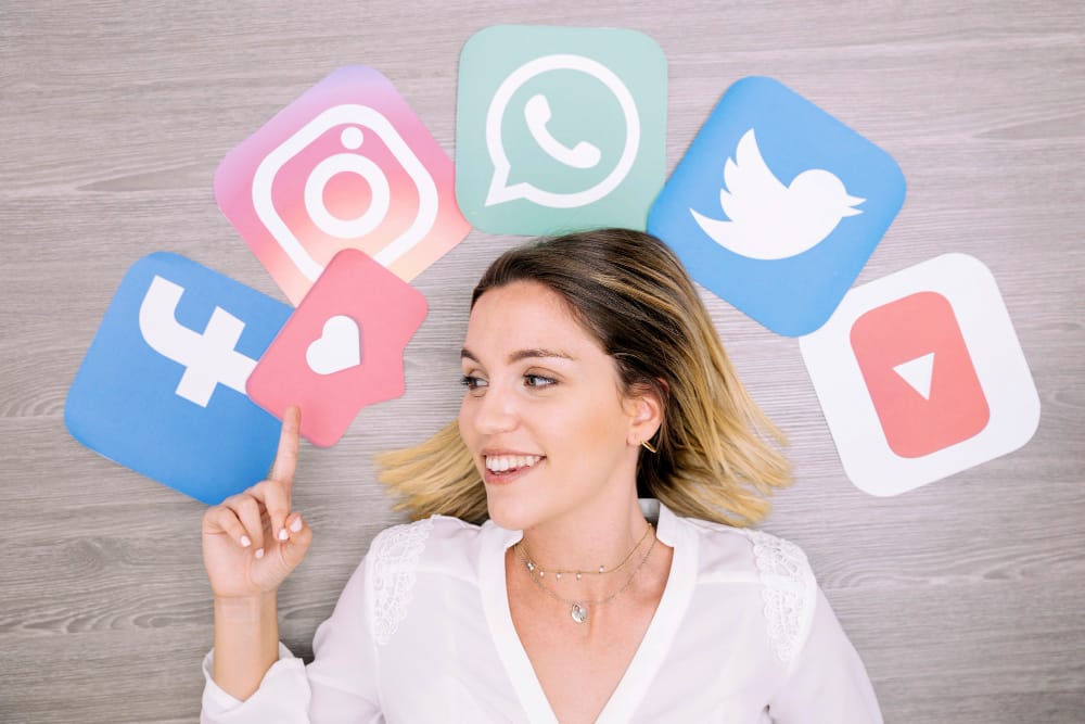 Smiling Woman Pointing Upward in Front of Wall With Social Networking Icons