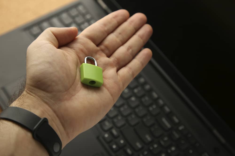 A Hand Holding a Green Padlock With a Laptop in Background